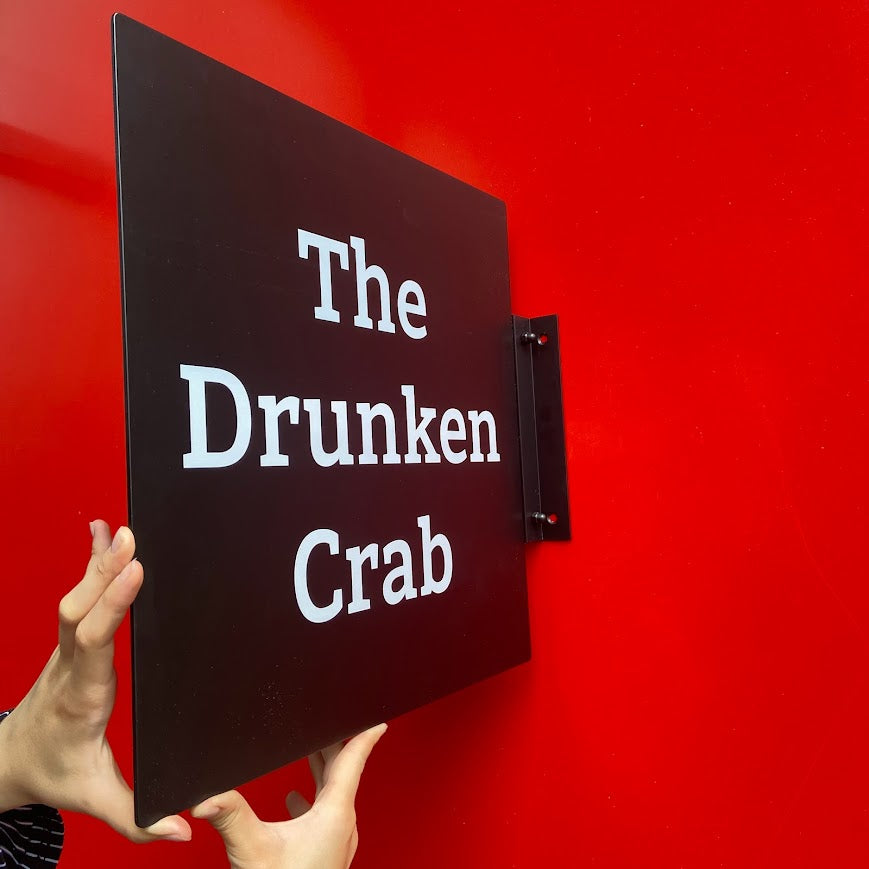 Siyah renkte kare duvar tabelası dış mekanda görüntüleniyor.