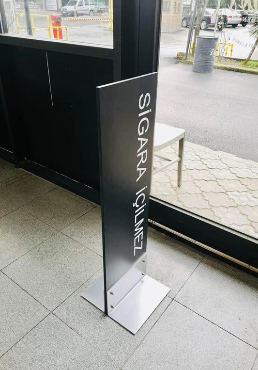 Ayakta duran metal levha üzerinde "Sigara İçilmez" uyarısı bulunan iç ve dış mekâna uygun ikaz tabelası.