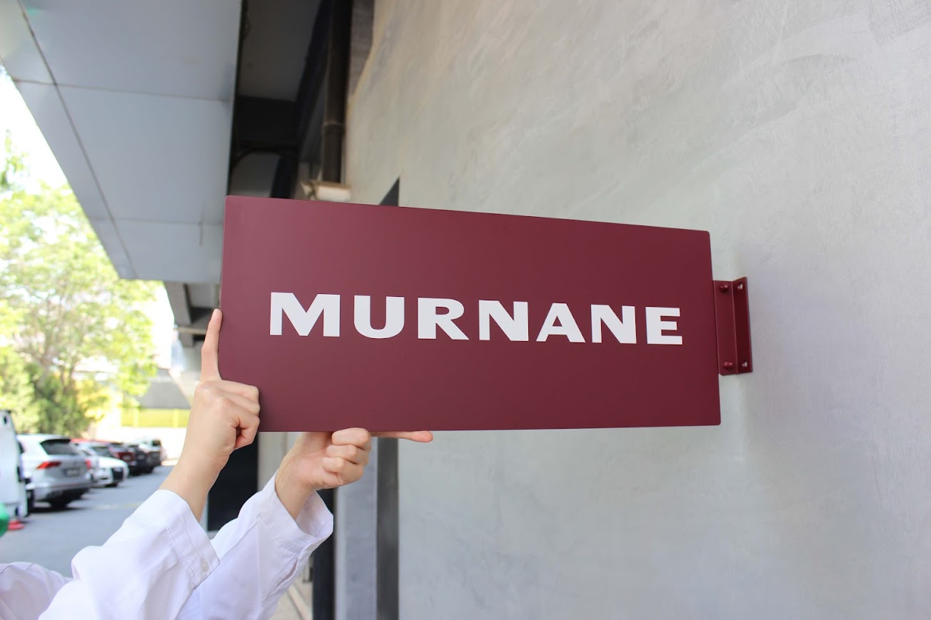 Dikdörtgen formlu metal tabela duvara monte edilmiş şekilde dış mekanda görüntüleniyor.