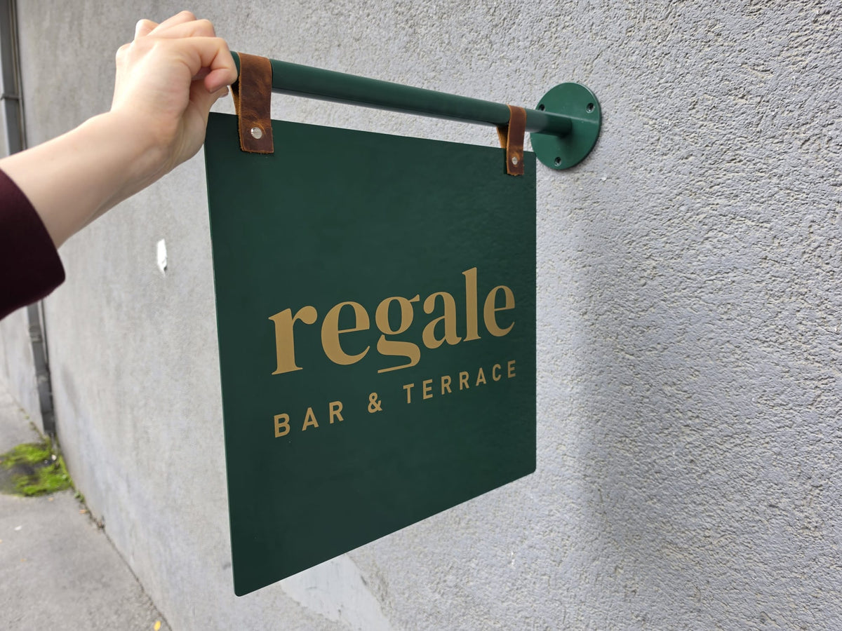 Regale Bar & Terrace logolu, deri askılı kare metal işletme tabelasının ön yüz görünümü