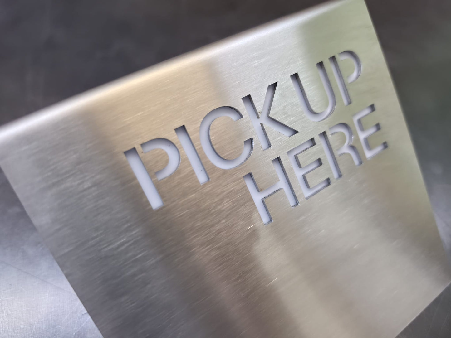 Paslanmaz çelik Pickup Here tabelasının dekupe yazı ve pleksi arka yüzey detayı