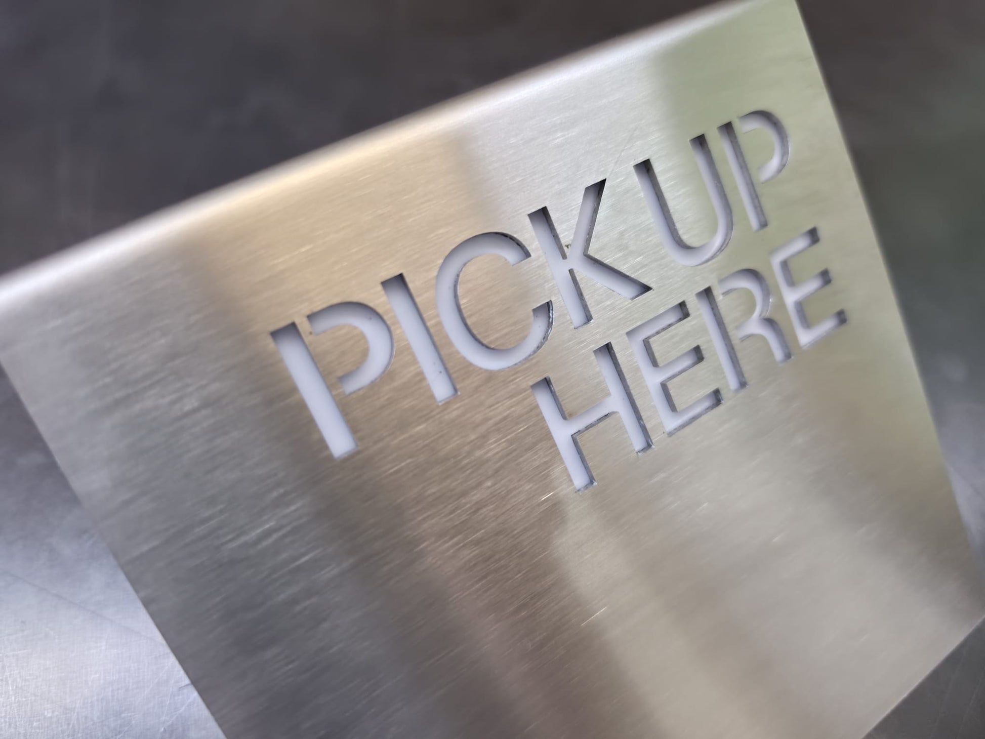 Paslanmaz çelik Pickup Here tabelasının dekupe yazı ve pleksi arka yüzey detayı