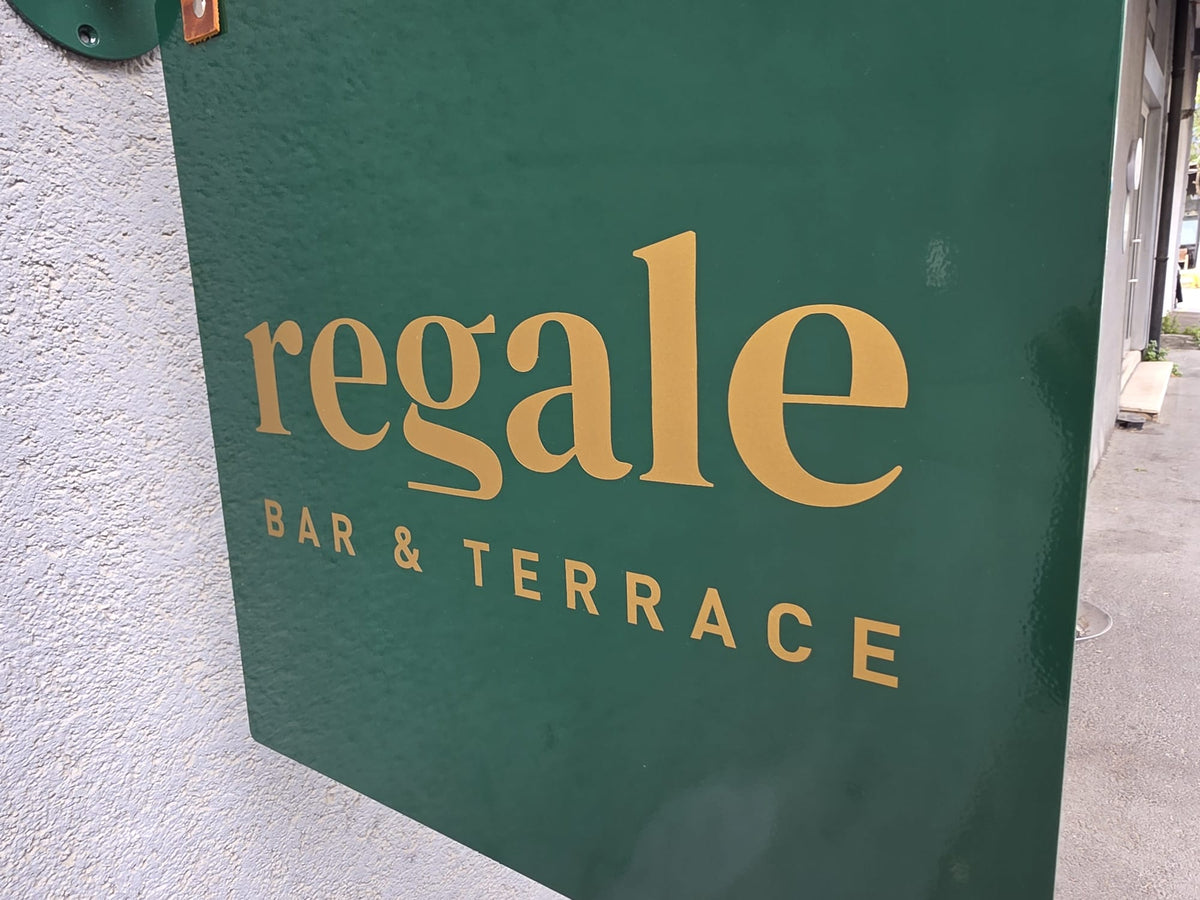 Koyu yeşil metal tabela yüzeyine uygulanan gold renk folyo işletme logosu ve yazı detayı