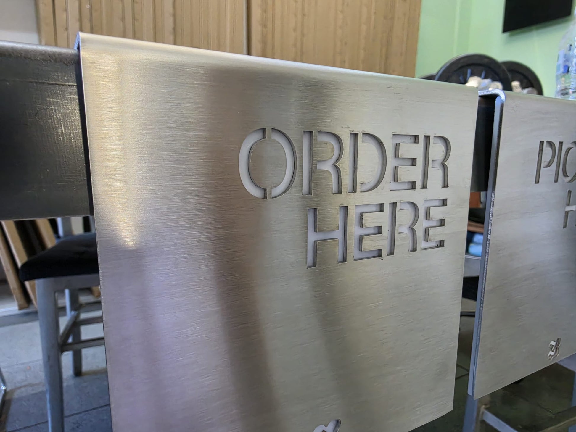 Dekupe Order Here yazılı paslanmaz çelik tezgah yönlendirme tabelası