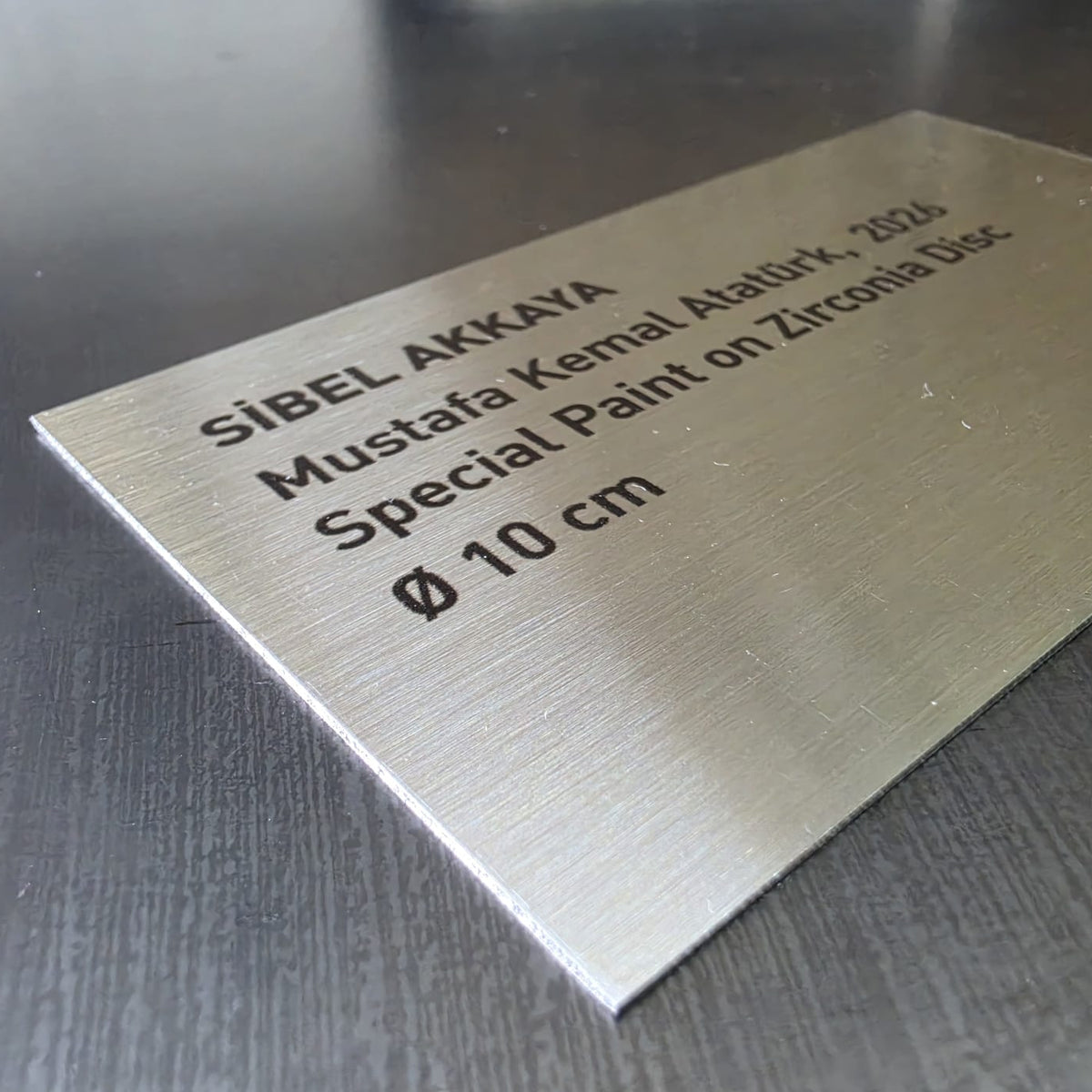 UV baskı tekniğiyle sanatçı adı, eser yılı, kullanılan teknik ve ölçü bilgilerinin uygulandığı metal künye